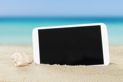 Closeup of tablet computer and shell on sand at beach