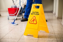 Low Section Of Worker Mopping Floor With Wet Floor Caution Sign On Floor