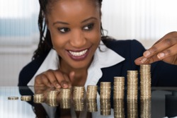Close-up Of A Smiling African Businesswoman Making Stack Of Coins