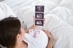 Pregnant Woman With Baby Shoes Looking At X-ray In Bedroom