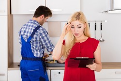 Young Frustrated Woman Looking At Huge Bill From Plumber Standing In Kitchen