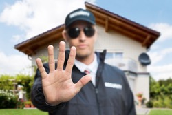 Close-up Of A Young Male Security Guard Making Stop Gesture In Front Of A House