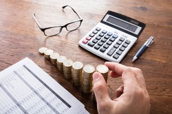 Person Stacking Coins With Calculator And Eyeglasses On Wooden Desk. Income Tax Rise Concept