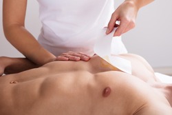 Close-up Of A Woman Waxing Man's Chest With Wax Strip