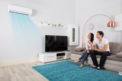 Smiling Young Couple Sitting On Sofa Using Air Conditioner