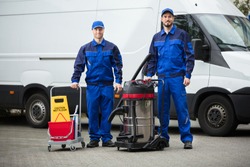Portrait Of Two Happy Male Janitors Standing With Cleaning Equipment