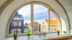 Close-up of arch semicircle window. View of old town of Riga, Latvia. Sill with flowers and decorative bicycle. Modern interior.