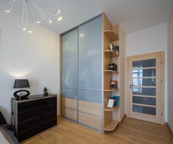 Modern interior of luxury bedroom. Stylish dark dresser. Glass sliding door wardrobe with wooden shelves. Home decor.
