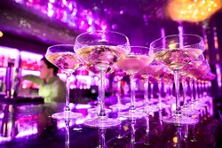 Glasses of champagne on bar counter with barman professional, which making cocktail drinks in background, soft focus