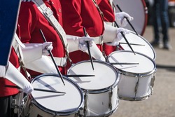 Drummers in red uniforms on a row at a spring parade with white gloves drumming on drums