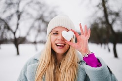 Attractive cheerful girl blonde heartbreaker bites a heart made of snow - romantic image of a woman