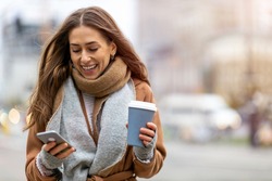 Smiling woman using mobile phone while having a coffee

