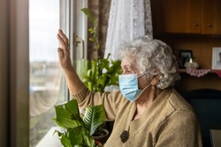 Senior woman with face mask looking out of window at home
