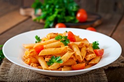 Penne pasta in tomato sauce with chicken, tomatoes decorated with parsley on a wooden background