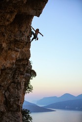 Young man climbing vertical cliff at sunset