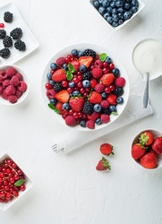 Bowl of healthy fresh berry fruit salad with cream on white background. Top view. Berries overhead closeup colorful assorted mix of strawberry, blueberry, raspberry, blackberry, red currant