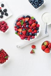 Bowl of healthy fresh berry fruit meal with cream on white background. Top view. Berries overhead closeup colorful assorted mix of strawberry, blueberry, raspberry, blackberry, red currant