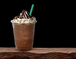 Frappuccino in take away cup on wooden table isolated on black