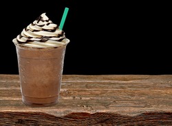 Iced coffee or frappuccino with cream in take away disposable cup on wooden table with black background.