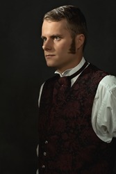 Shadowy portrait of a young man in vintage Victorian attire in front of a dark gray wall.