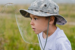 A little boy on the field is looking closely at a spider's web at sunrise in the fog. Young naturalist. Observation of the nature of the child