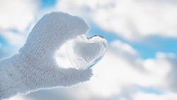 frozen icy heart hand, winter background against clear blue sky and clouds, concept love, romantic, February 14, Valentine's day.
