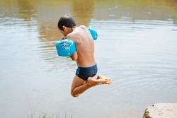 Children have fun and play in the water in a pond outside the city in the village on summer holidays. happy boy jumps into the water splashing swimming in the lake