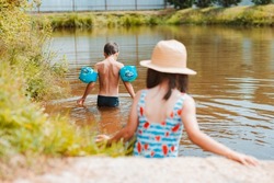 Children have fun and play in the water in a pond outside the city in the village on summer holidays. happy boy inflatable circle and armbands splashing swimming in the lake