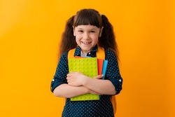 portrait of a schoolgirl girl wearing glasses with a backpack textbooks yellow background. The concept of back to school, training, education, free space, copy space