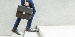 Businessman with black briefcase in hand walking up on stairs. business goal, improvement, progress, Increase and growth concept. Outdoor closeup shot. in grey wall copy space.