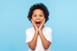 Oh my god, wow! Portrait of funny amazed preschool boy looking at camera with shocked astonished expression and keeping hands on face, screaming in surprise. studio shot isolated on blue background