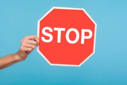 Closeup of male hand holding Stop symbol, showing red traffic sign, warning about problems, concept of ban, denial, prohibited to go, forbidden way. indoor studio shot isolated on blue background
