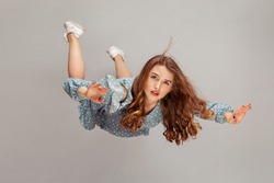 Beautiful girl levitating in mid-air, falling down and her hair messed up soaring from wind, model flying hovering with dreamy peaceful expression. indoor studio shot isolated on gray background