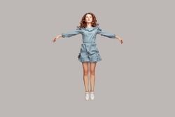 Full length happy calm pretty girl in vintage ruffle dress levitating hovering in mid-air with raised hands as wings, jumping trampoline or flying up. indoor studio shot isolated on gray background