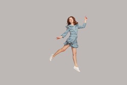 Happy delicate girl in vintage ruffle dress levitating with ballet dance move, hovering in mid-air and smiling joyfully, jumping trampoline, flying up. indoor studio shot isolated on gray background
