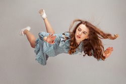 Beautiful girl levitating in mid-air, falling down and her hair messed up soaring from wind, model flying hovering with dreamy peaceful expression. indoor studio shot isolated on gray background