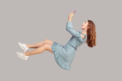 Hovering in air. Surprised shocked girl ruffle dress levitating with mobile phone, chatting online in social network amazed by unbelievable news message, surfing web while flying. studio shot isolated