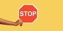 Closeup of male hand holding octagonal red Stop symbol, ban concept, arm showing traffic sign, prohibition concept, forbidden way, no access. Indoor studio shot isolated on yellow background.