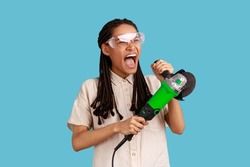 Portrait of enthusiastic woman with dreadlocks working with grinder saw, yelling with excitement, wearing white shirt and protective glasses. Indoor studio shot isolated on blue background.