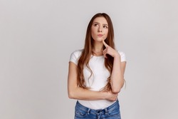 Portrait of standing with thoughtful serious smart expression, pondering answer, having doubts and suspicion, wearing white T-shirt. Indoor studio shot isolated on gray background.