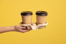 Profile side view closeup of woman hand holding and showing cup of hot takeaway mug drink in hand, coffee break at work. Indoor studio shot isolated on yellow background.