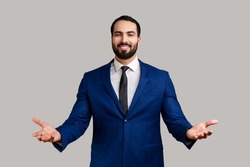 Wide open hug. Nice to meet you. Bearded businessman standing with wide raised arms and welcoming or sharing, wearing official style suit. Indoor studio shot isolated on gray background.