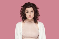 Portrait of surprised shocked sad attractive woman with curly hair wearing casual style outfit looking at camera with upset eyes. Indoor studio shot isolated on pink background.