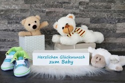 Teddy bear and gifts for the baby with the text herzlichen Glückwunsch zum Baby. Herzlichen Glückwunsch zum Baby translates to congratulations on the baby.