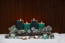 Fourth Advent: Green Advent candles with Christmas decorations in the snow.