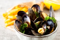 Mussels with herbs in a bowl with lemon and French fries on a white wooden board. Seafood. Food at the shore of the French Sea. Dark background