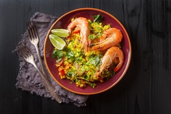 Spanish paella with seafood on the red teralke with lime. Delicious lunch on the shore of the sea shrimp. Dark wood background