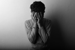 Black and white image of a young boy feeling shame covering his face with hands.One light studio shot with shadow