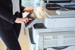Woman standing and pressing button on a copy machine in the office