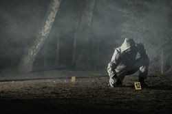 Looking For Traces and Crime Evidence Markers Placing by Forensic Officer in Hazmat Suit and Gloves. Dark Foggy Forest. Crime Scene Theme Concept.